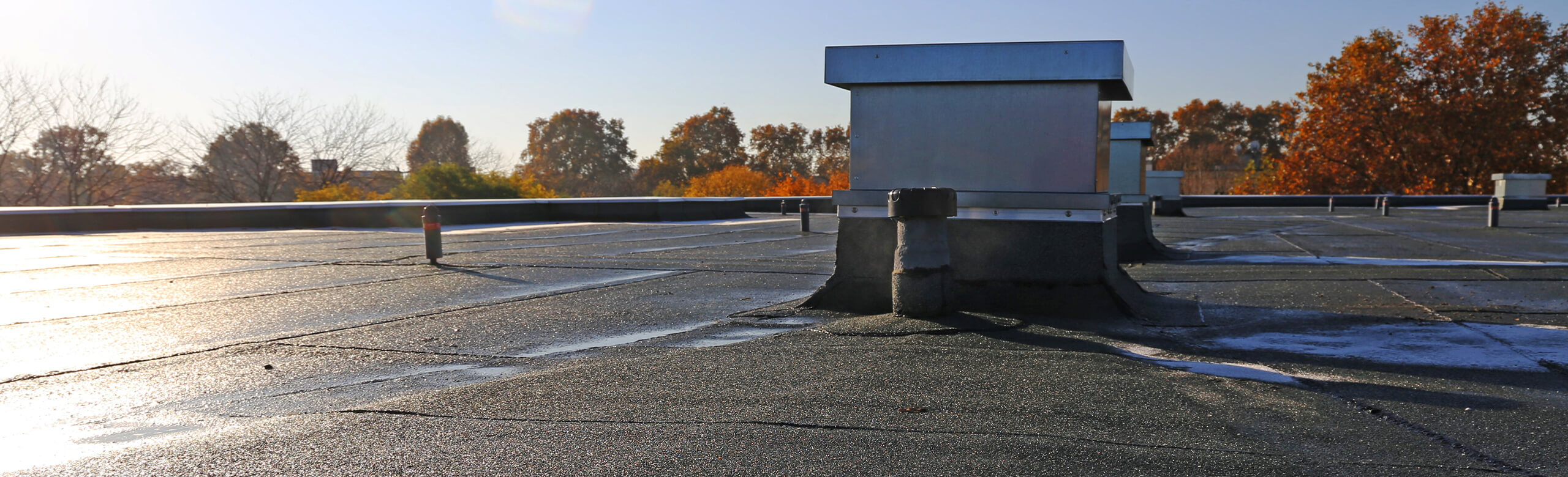 Flachdach mit Dachaufbauten und abgedichteten Anschlüssen im Herbstlicht